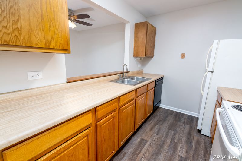 Kitchen with wood cabinets, stainless double sink, black dishwasher and white refrigerator, Oriole Court apartment 2A