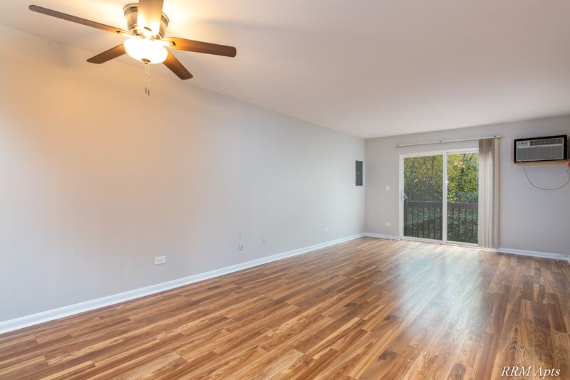 Living room with wood laminate floor, ceiling fan, sliding glass door and a wall air conditioner, Oriole Court apartment 2B