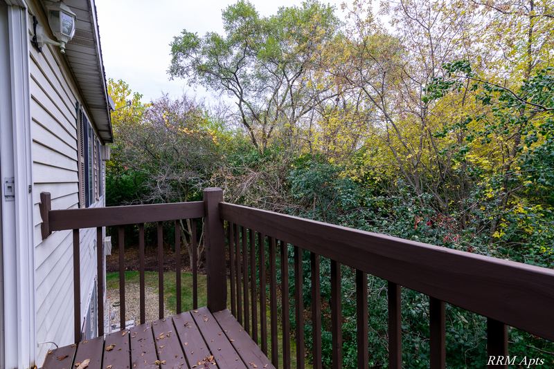 Balcony with brown wood railing overlooking trees beside the building's siding, Oriole Court apartment 2B