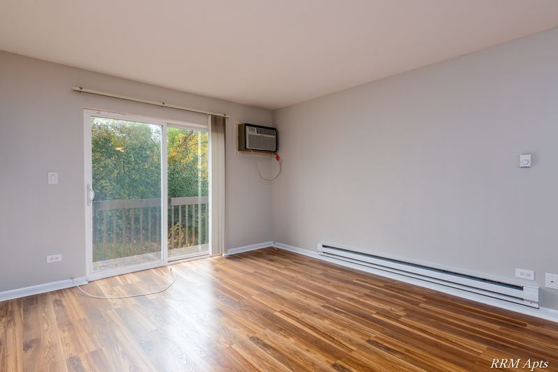 Living room with wood laminate floor, sliding glass door with trees outside and baseboard heat, Oriole Court apartment 2B