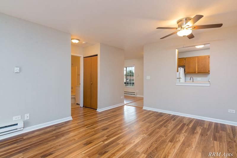 Living room with wood laminate floor, ceiling fan, wood-door hallway and kitchen pass-through, Oriole Court apartment 2B