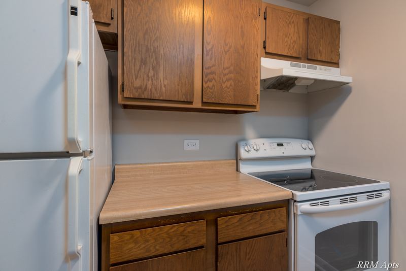 Kitchen with white refrigerator, wood cabinets and white electric stove under a range hood, Oriole Court apartment 2B