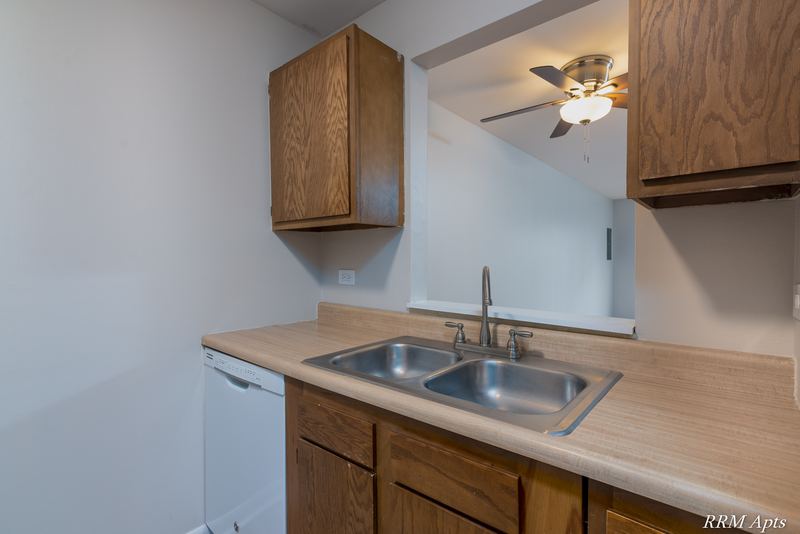Kitchen with wood cabinets, stainless sink, white dishwasher and living room pass-through, Oriole Court apartment 2B