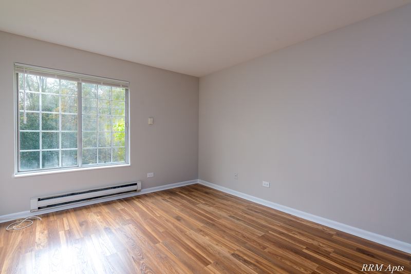 Bedroom with wood laminate floor, a grid-pane window with trees outside and baseboard heat, Oriole Court apartment 2B