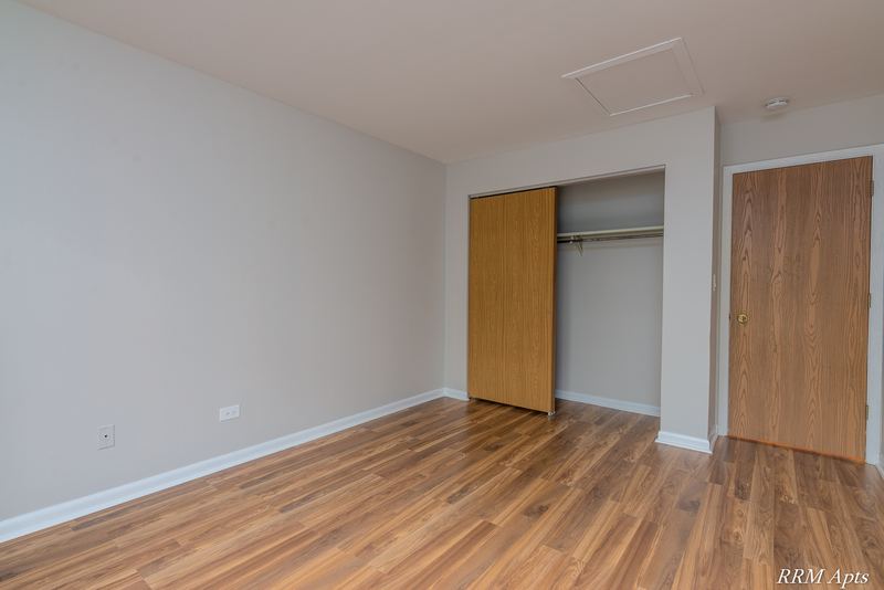 Bedroom with wood laminate floor, an open closet with wood bifold doors and a wood door, Oriole Court apartment 2B