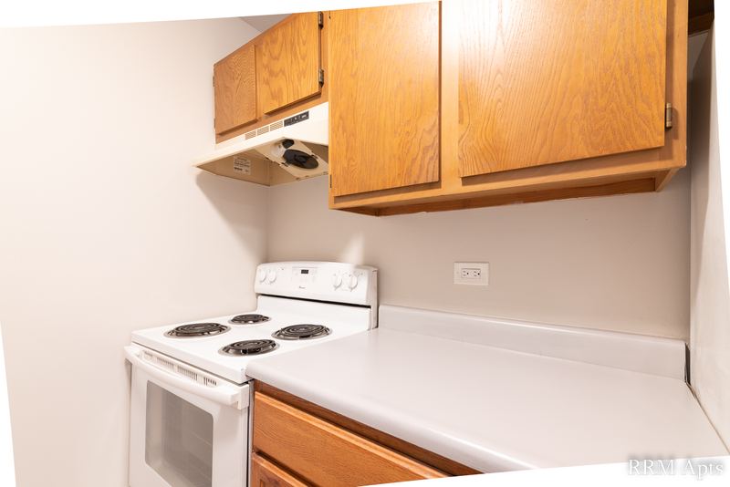 Kitchen with wood cabinets, white electric stove under a range hood and light counter, Oriole Court apartment 2C