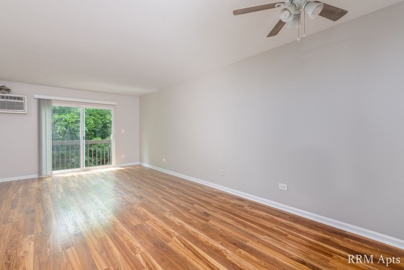 Living room with wood laminate floor, ceiling fan, sliding glass door and wall air conditioner, Oriole Court apartment 2C