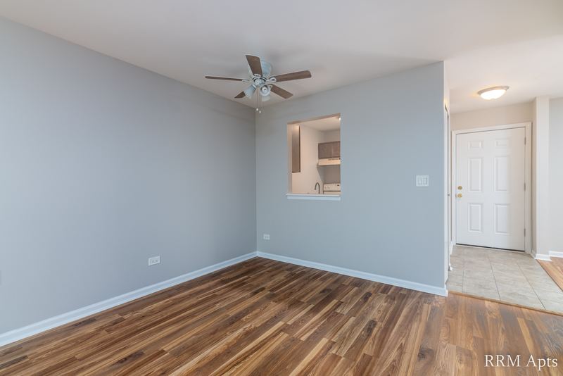 Living room with wood laminate floor, ceiling fan, kitchen pass-through and white entry door, Oriole Court apartment 2C