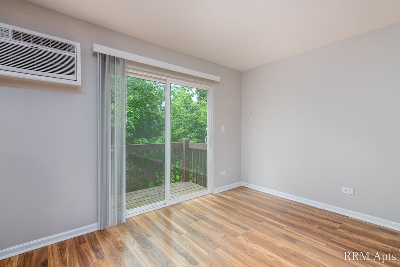 Living room with wood laminate floor, sliding door to trees and a wall air conditioner above it, Oriole Court apartment 2C