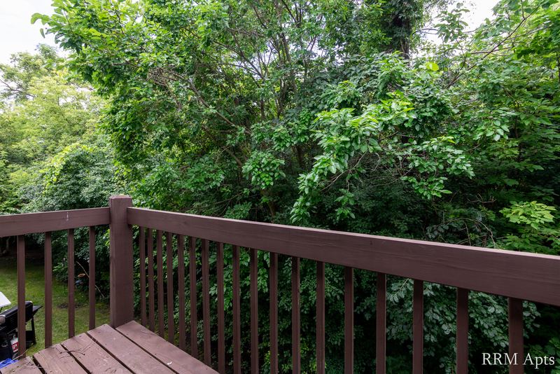 Balcony with brown wood railing and a view of leafy green trees, Oriole Court apartment 2C