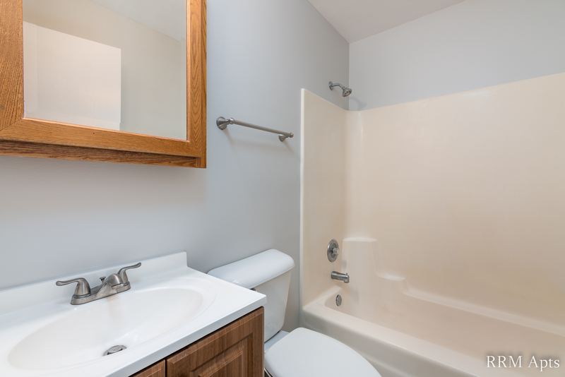 Bathroom with white vanity, wood-framed medicine cabinet, white tub surround and toilet, Oriole Court apartment 2C