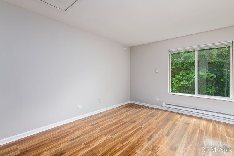 Bedroom with wood laminate floor, a window with trees outside and baseboard heat, Oriole Court apartment 2C