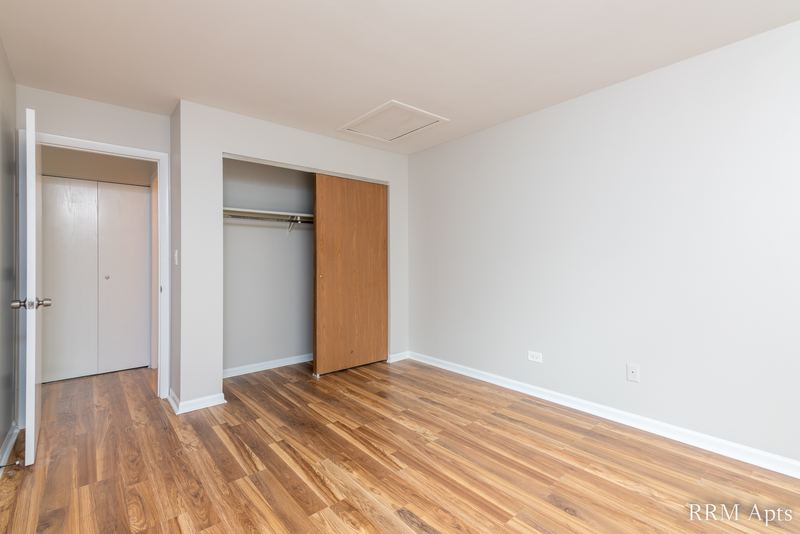 Bedroom with wood laminate floor, an open closet with wood bifold door and a white door, Oriole Court apartment 2C
