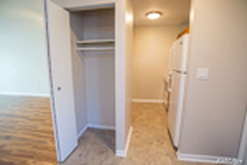 Hallway with white bifold closet doors, tile floor and the kitchen refrigerator beyond, Oriole Court apartment 2D