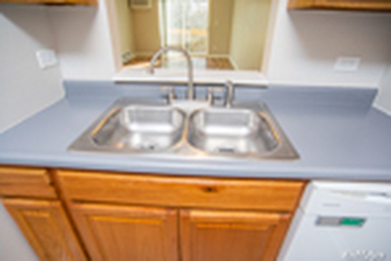 Kitchen with wood cabinets, stainless double sink, white dishwasher and gray counter, Oriole Court apartment 2D