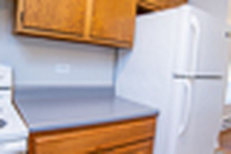 Kitchen corner with oak cabinets, gray counter and a white refrigerator, Oriole Court apartment 2D