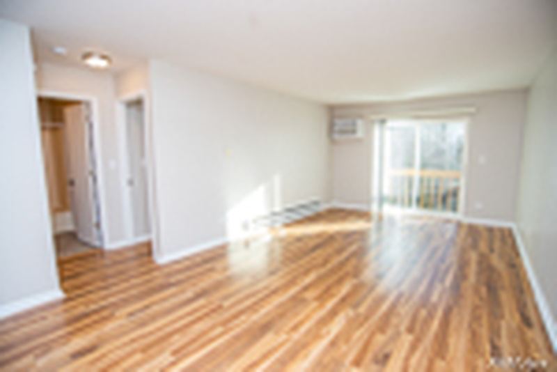 Living room with wood laminate floor, sliding glass door and a hallway with white doors, Oriole Court apartment 2D