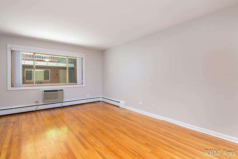 Living room with wood floor, wide window facing a brick building and a wall air conditioner, Park Avenue apartment 603 103