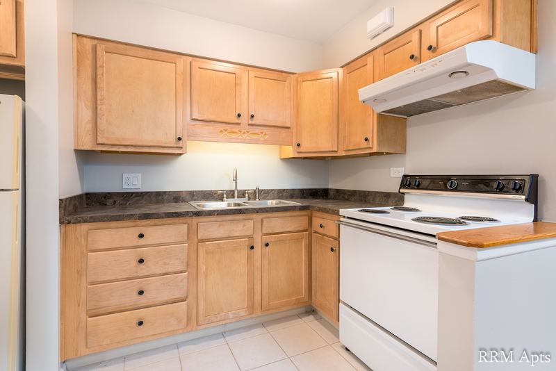 Kitchen with light oak cabinets, white stove and refrigerator and a dark speckled counter, Park Avenue apartment 603 103