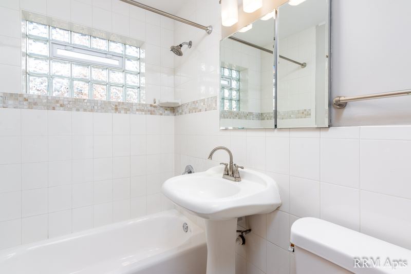 Bathroom with white tile tub surround, glass block window, pedestal sink and a mirror, Park Avenue apartment 603 103