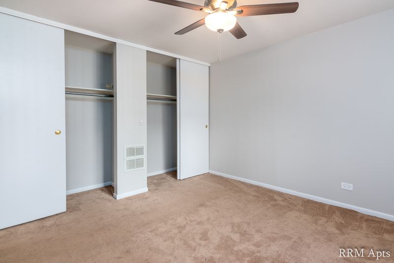 Bedroom with beige carpet, ceiling fan and a wide closet with open sliding doors, Park Avenue apartment 603 103