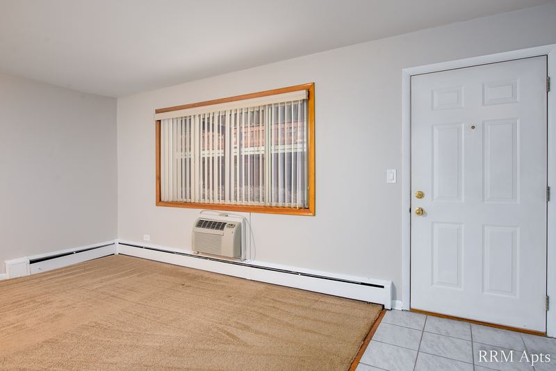 Living room with beige carpet, white entry door, blinds and a wall air conditioner, Park Avenue apartment 603 104