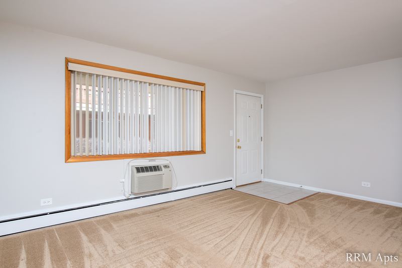 Living room with beige carpet, oak-trimmed window, wall air conditioner and a white door, Park Avenue apartment 603 104