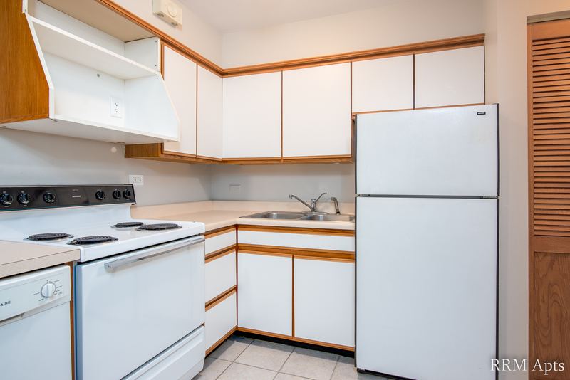 Kitchen with white oak-trimmed cabinets, white stove, refrigerator and a louvered door, Park Avenue apartment 603 104