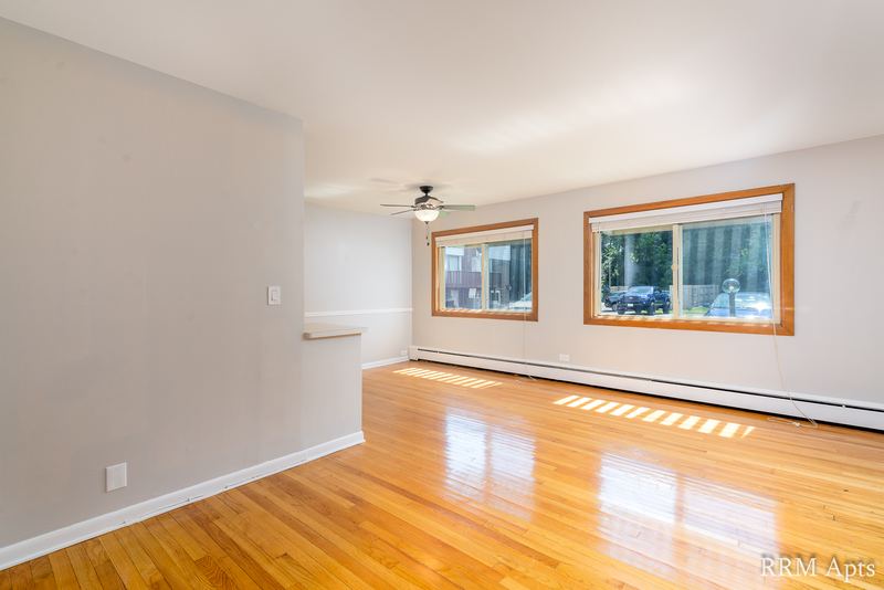 Living room with wood floor, ceiling fan, two windows with trees and a baseboard heater, Park Avenue apartment 603 106