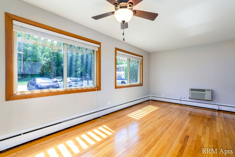 Living room with wood floor, ceiling fan, oak-trimmed windows and a wall air conditioner, Park Avenue apartment 603 106