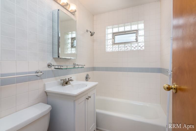 Bathroom with white tile tub surround, glass block window, white vanity and mirror, Park Avenue apartment 603 106