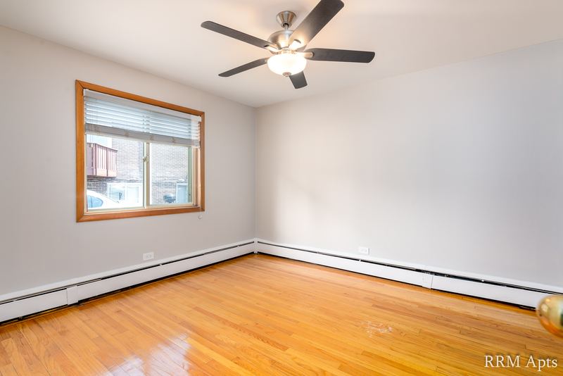 Bedroom with wood floor, ceiling fan, oak-trimmed window and a baseboard heater, Park Avenue apartment 603 106