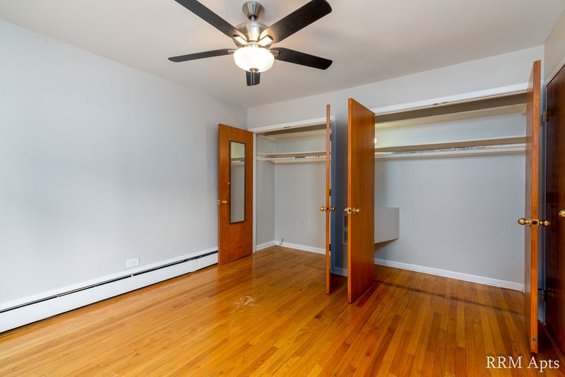 Bedroom with wood floor, ceiling fan, open closet doors and an oak door, Park Avenue apartment 603 106