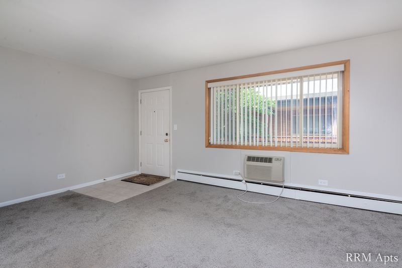 Living room with gray carpet, white entry door, window blinds and a wall air conditioner, Park Avenue apartment 603 205