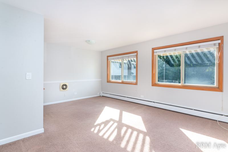 Living room with beige carpet, two oak-trimmed windows with trees and a baseboard heater, Park Avenue apartment 603-206
