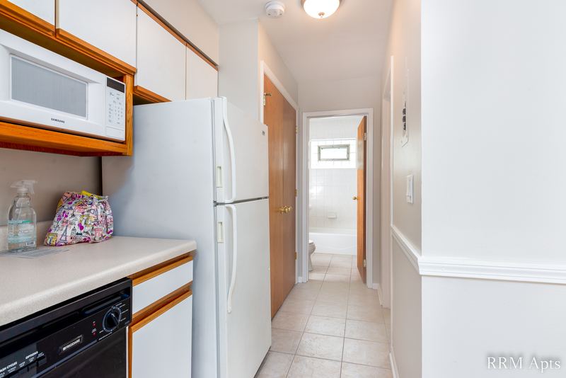 Kitchen with white refrigerator, microwave, black dishwasher and a hallway to the bathroom, Park Avenue apartment 603-206