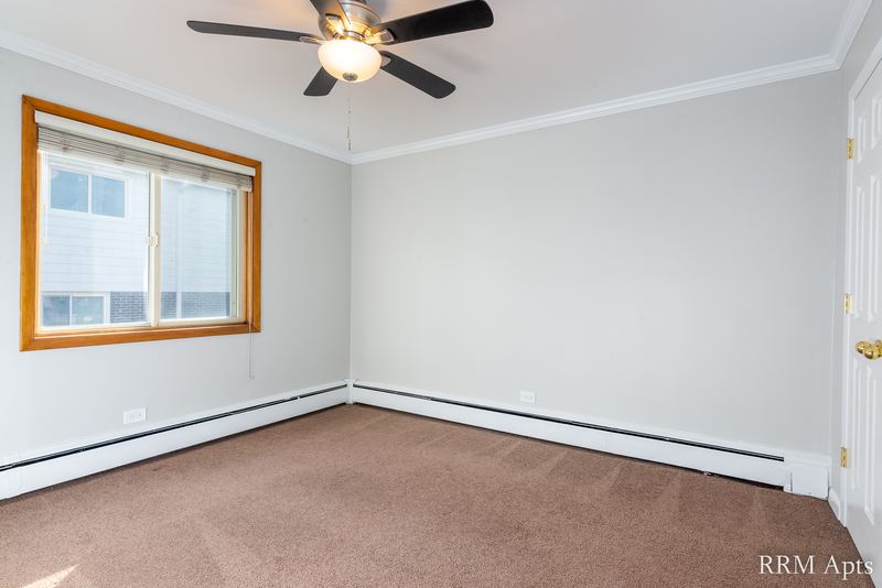 Bedroom with beige carpet, ceiling fan, oak-trimmed window and a baseboard heater, Park Avenue apartment 603-206