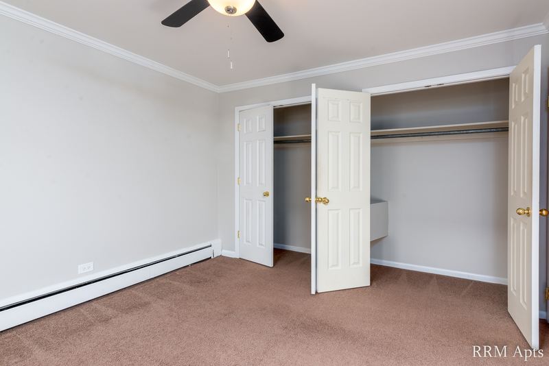 Bedroom with beige carpet, ceiling fan, open closet doors and a baseboard heater, Park Avenue apartment 603-206