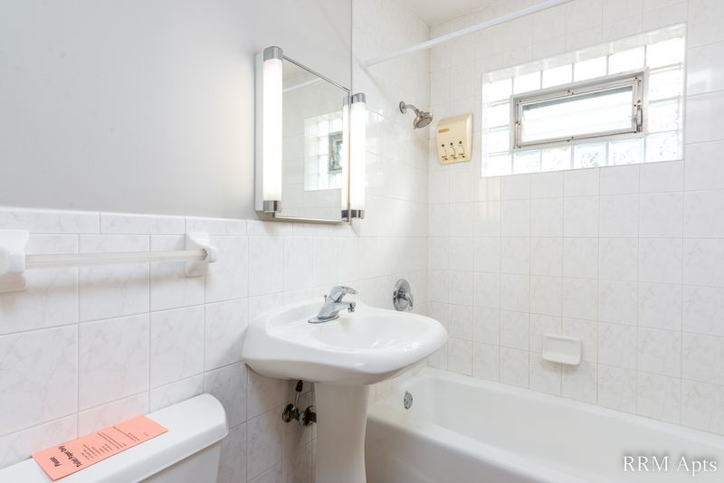Bathroom with white tile walls, glass block window, pedestal sink, mirror and tub, Park Avenue apartment 603-206