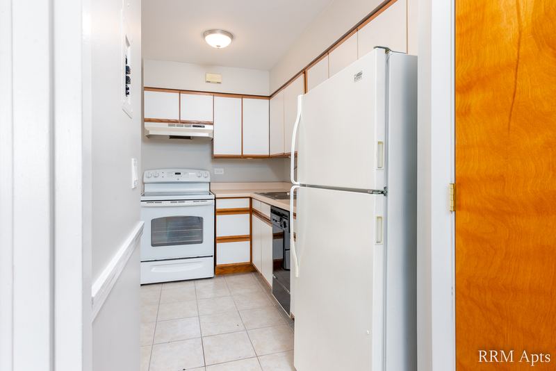 Kitchen with white cabinets, white stove and refrigerator, tile floor and an oak door, Park Avenue apartment 603-206