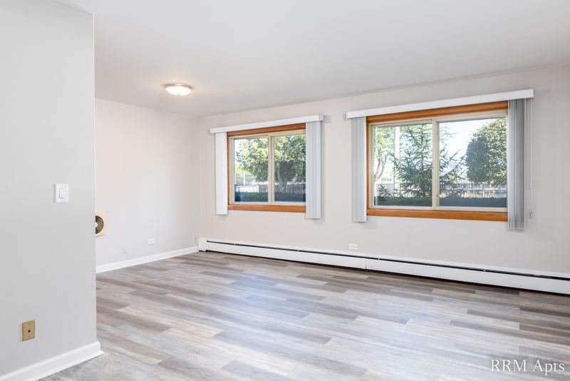 Living room with wood-look floor, two oak-trimmed windows with trees and a baseboard heater, Park Avenue apartment 607 101