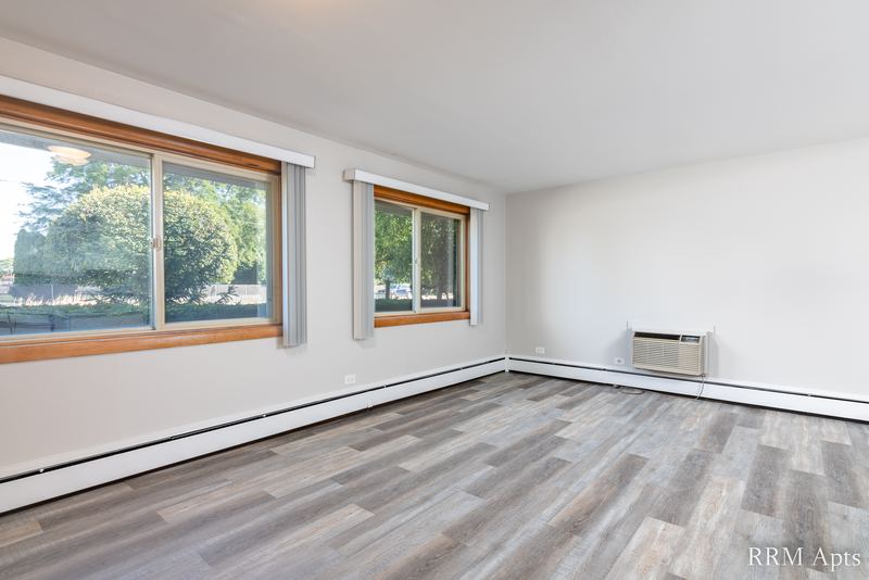 Living room with wood-look floor, two windows with trees and a wall air conditioner, Park Avenue apartment 607 101