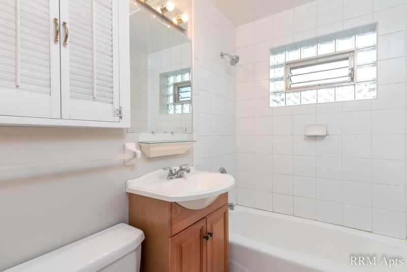 Bathroom with white tile tub surround, glass block window, oak vanity and mirrored cabinet, Park Avenue apartment 607 101