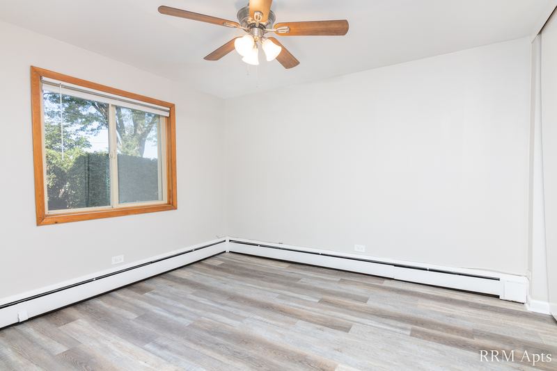 Bedroom with wood-look floor, ceiling fan, window with trees and a baseboard heater, Park Avenue apartment 607 101
