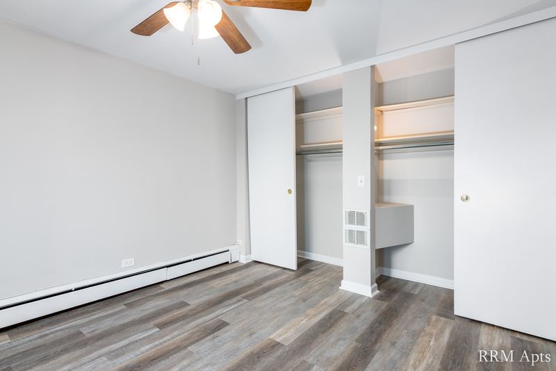 Bedroom with wood-look floor, ceiling fan and two open closets with shelves, Park Avenue apartment 607 101