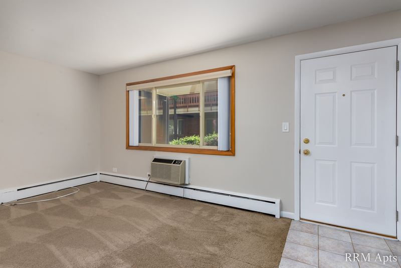 Living room with beige carpet, window, wall air conditioner and a white entry door, Park Avenue apartment 607 103