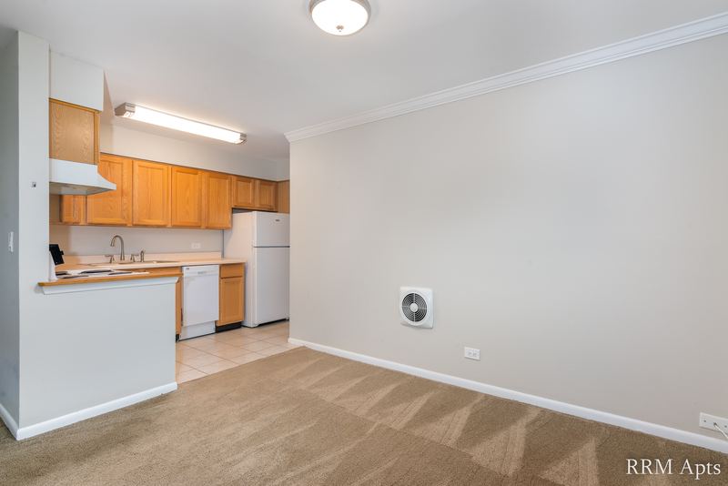 Living room with beige carpet, a round wall vent and a view into the oak-cabinet kitchen, Park Avenue apartment 607 103
