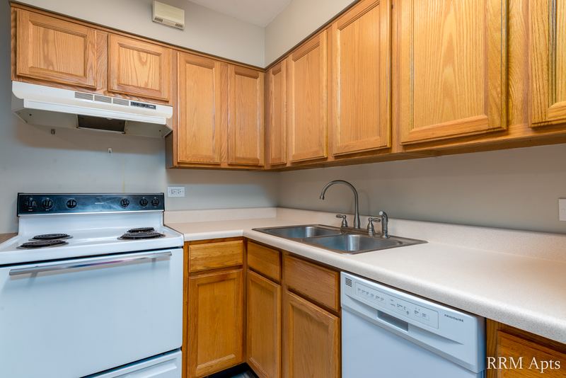 Kitchen with oak cabinets, white stove, white dishwasher, range hood and a double sink, Park Avenue apartment 607 103