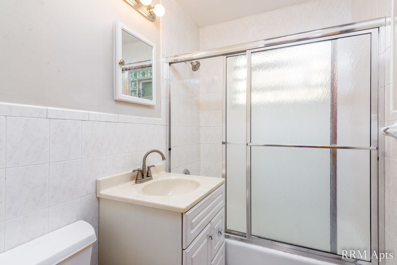 Bathroom with white tile walls, sliding glass tub doors, oak vanity and a mirror, Park Avenue apartment 607 103