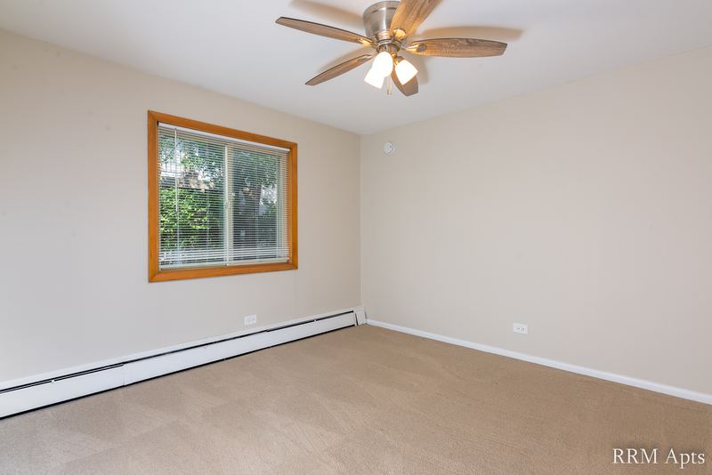 Bedroom with beige carpet, ceiling fan, window with trees and a baseboard heater, Park Avenue apartment 607 103